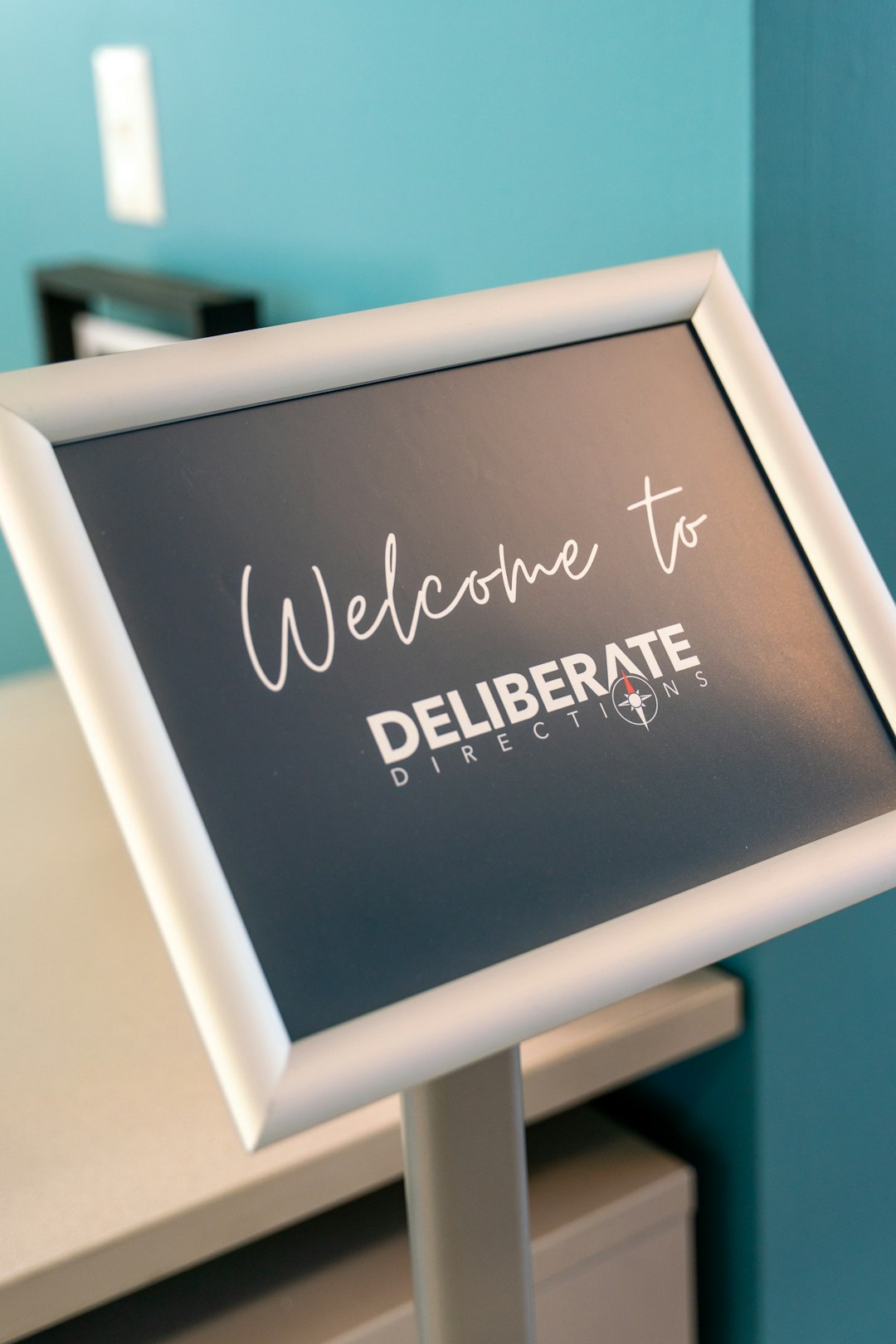 A clean, modern welcome sign greets guests entering the Deliberate Directions office in downtown Boise. Framed in white and set against a teal accent wall, the sign reflects the brand’s professional tone and focus on purposeful client experiences. It sets the stage for what visitors can expect—clarity, guidance, and a space built for growth.